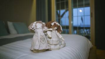Two dolls on a bed in a room with a large window and a view of the sky.
