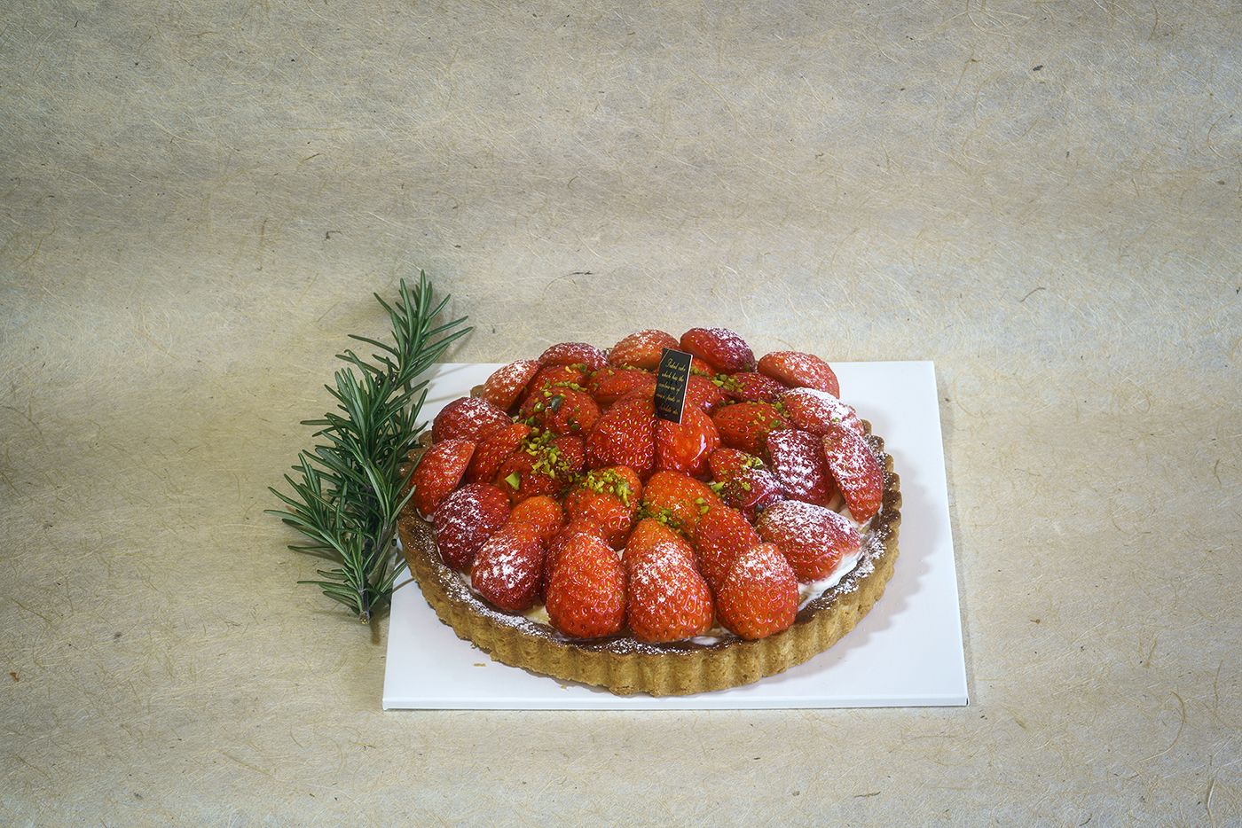 A strawberry tart on a white plate with a sprig of rosemary beside it.