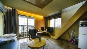 A compact living space with a sofa, a small round table, a television, and a sliding door leading to a balcony. - Tongyeong MongDol House (Tongyeong)
