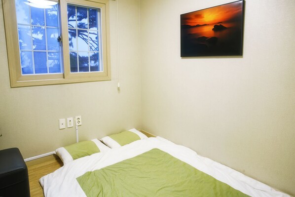 A small, clean room with a single bed, a window, and a painting on the wall.