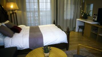 Hotellihuone, jossa on suuri sänky, työpöytä, tuoli, lamppu ja pieni kasvi pyöreällä pöydällä.