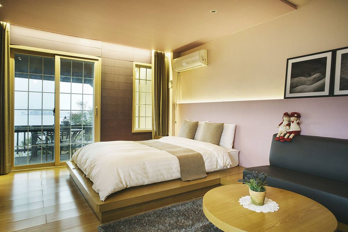 A hotel room with a bed, a sofa, a round table with a plant, and a balcony with a view.