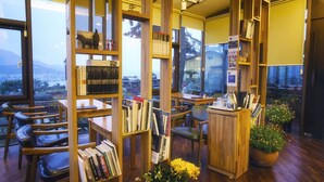 A cozy library with wooden bookshelves, comfortable seating, and a view of the outdoors. - Tongyeong MongDol House (Tongyeong)