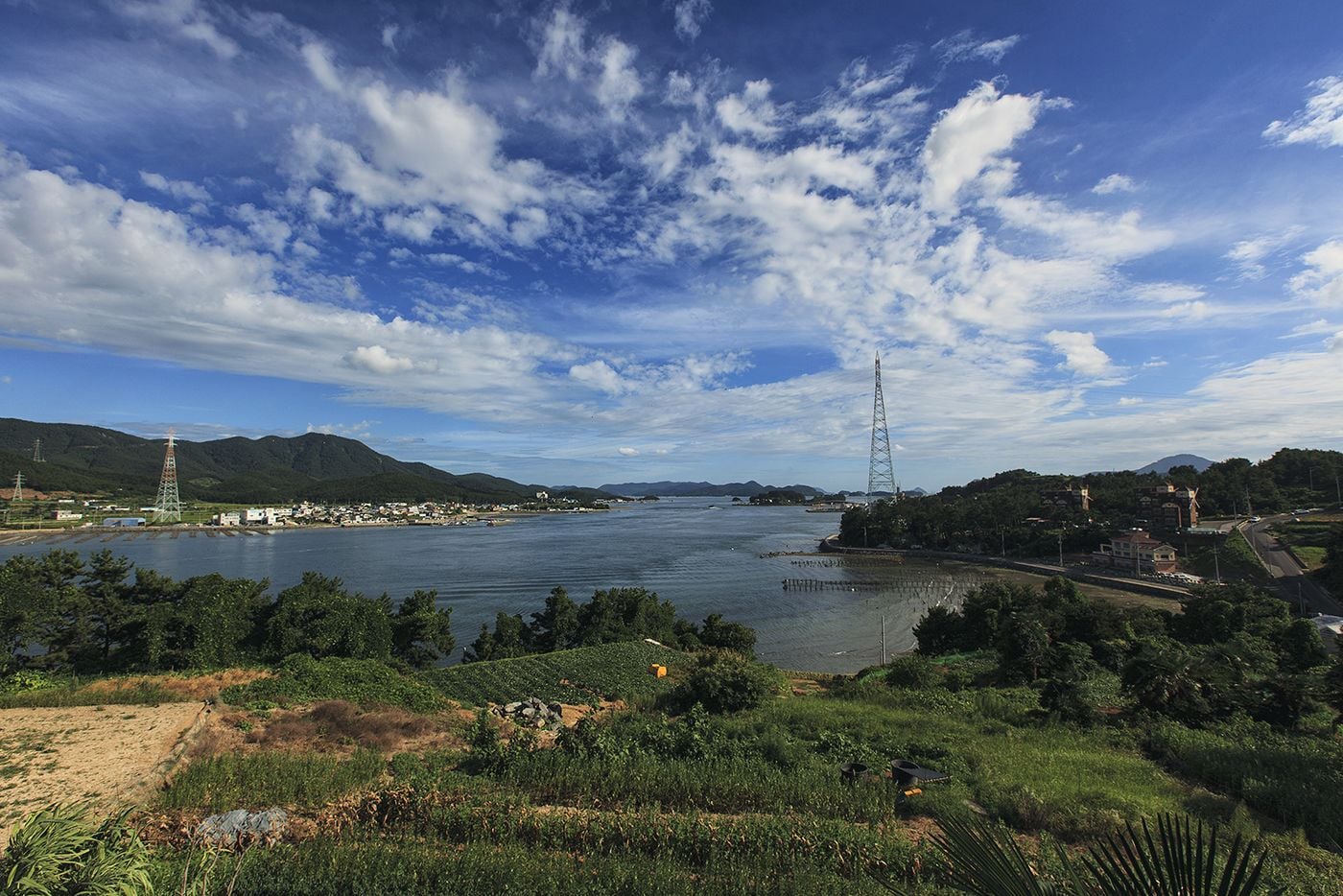 A coastal landscape with a river, hills, and a tall communication tower.