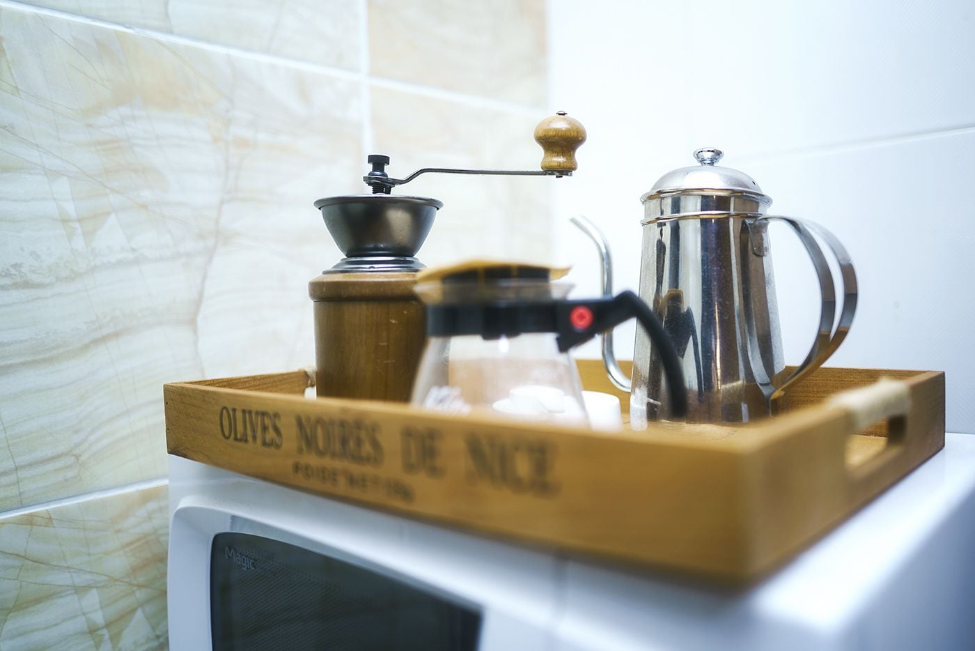 A coffee maker and a French press on a wooden tray with text, placed on a white appliance.
