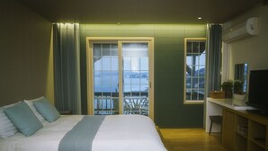 A bedroom with a bed, a desk with a TV, and a view of the outdoors through a window. - Tongyeong MongDol House (Tongyeong)