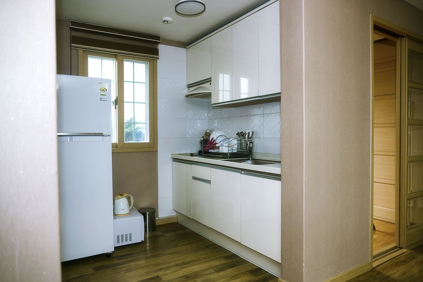 Una cocina compacta con armarios blancos, horno empotrado y ventana.