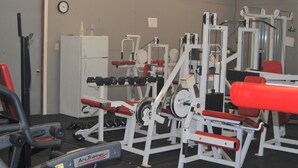 A gym with various exercise equipment, a clock on the wall, and a door on the left. - The Golf Inn at QC Resort and RV (Hartselle)