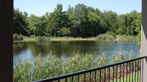 A view of a lake surrounded by dense trees, with a railing in the foreground. - The Golf Inn at QC Resort and RV (Hartselle)