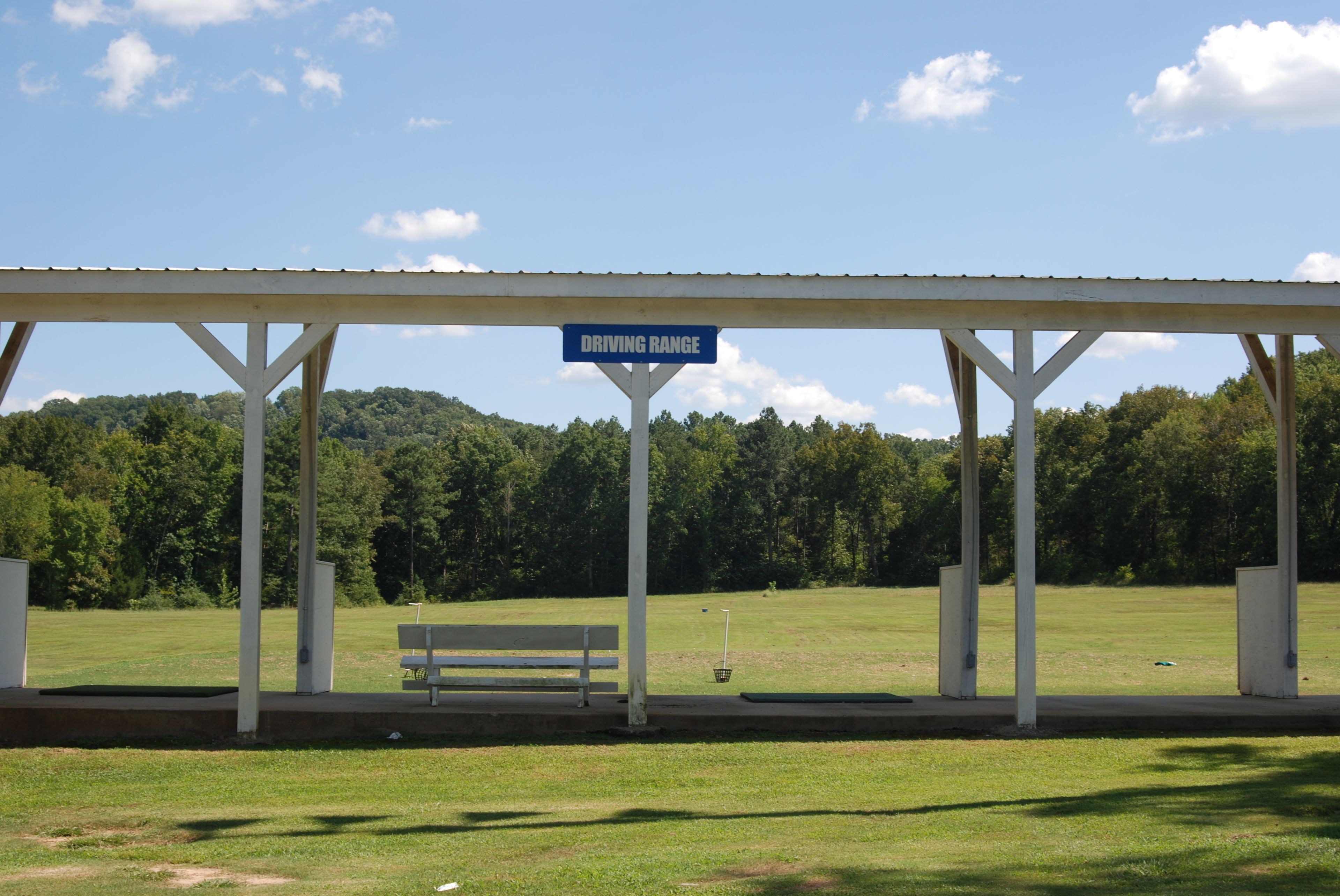 A covered area with a sign reading "DRIVING RANGE" and a bench.