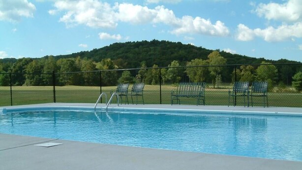 A swimming pool with a metal ladder, surrounded by a fence and several green chairs. - The Golf Inn at QC Resort and RV (Hartselle)