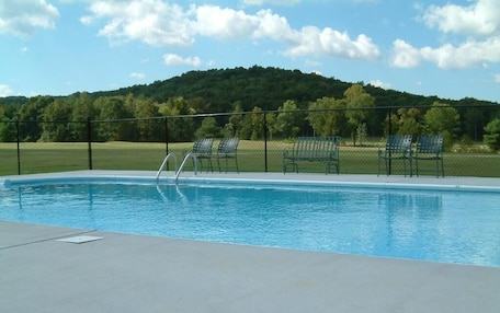 A swimming pool with a metal ladder, surrounded by a fence and several green chairs.