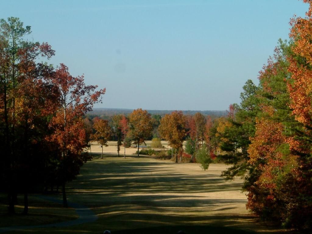 A golf course with trees in autumn colors, a clear sky, and a distant view.
