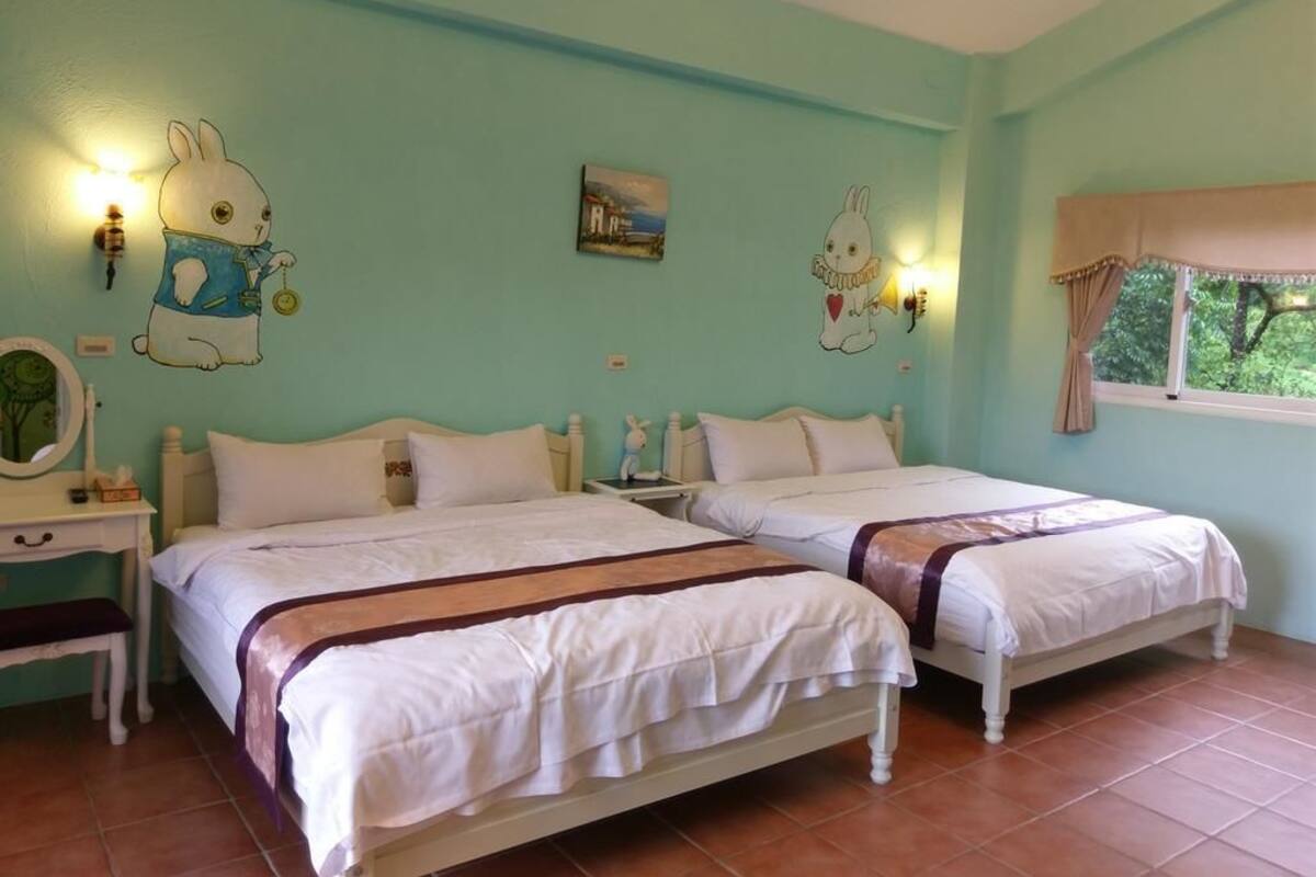 Une chambre avec deux lits, une table de chevet, une commode et des décorations murales, notamment des dessins de lapins.