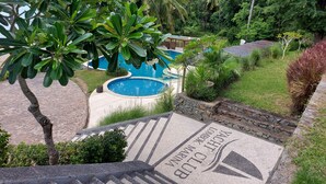 Un’area piscina con un vialetto in pietra che conduce alla vasca, circondata da vegetazione lussureggiante e palme.
