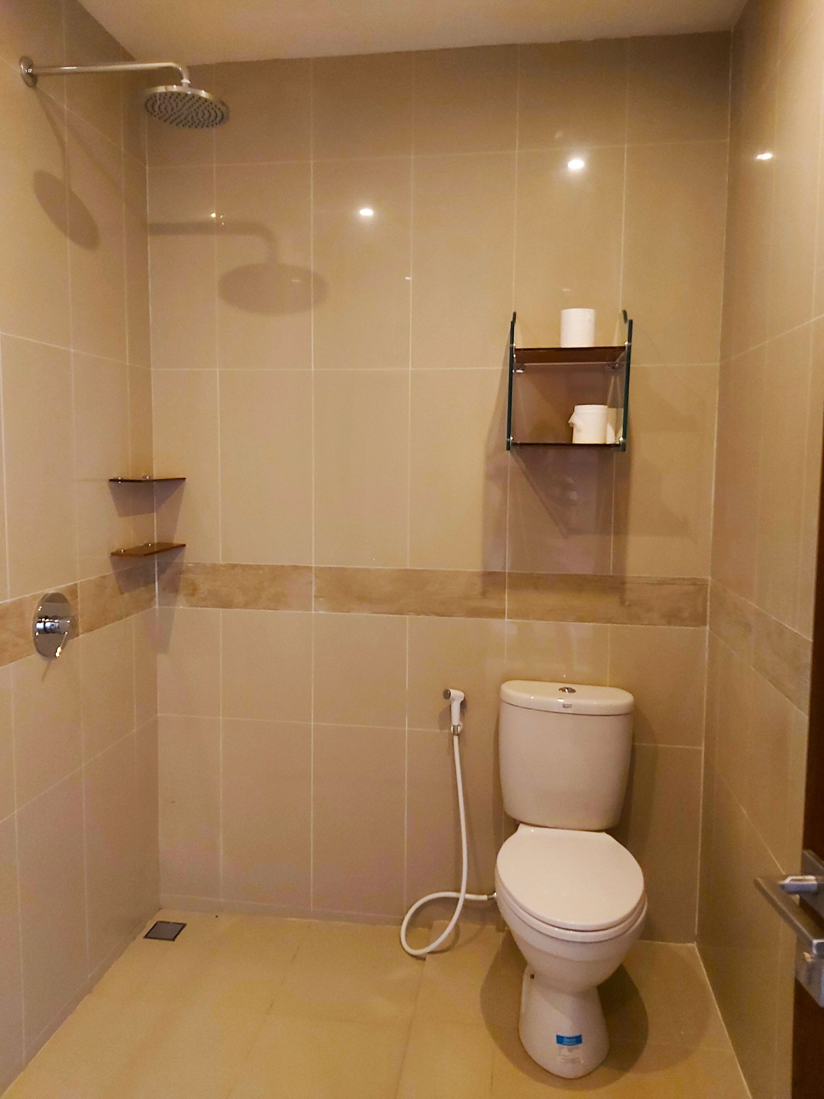 Un baño pequeño, con azulejos, que incluye una ducha, inodoro y estante con artículos de aseo.
