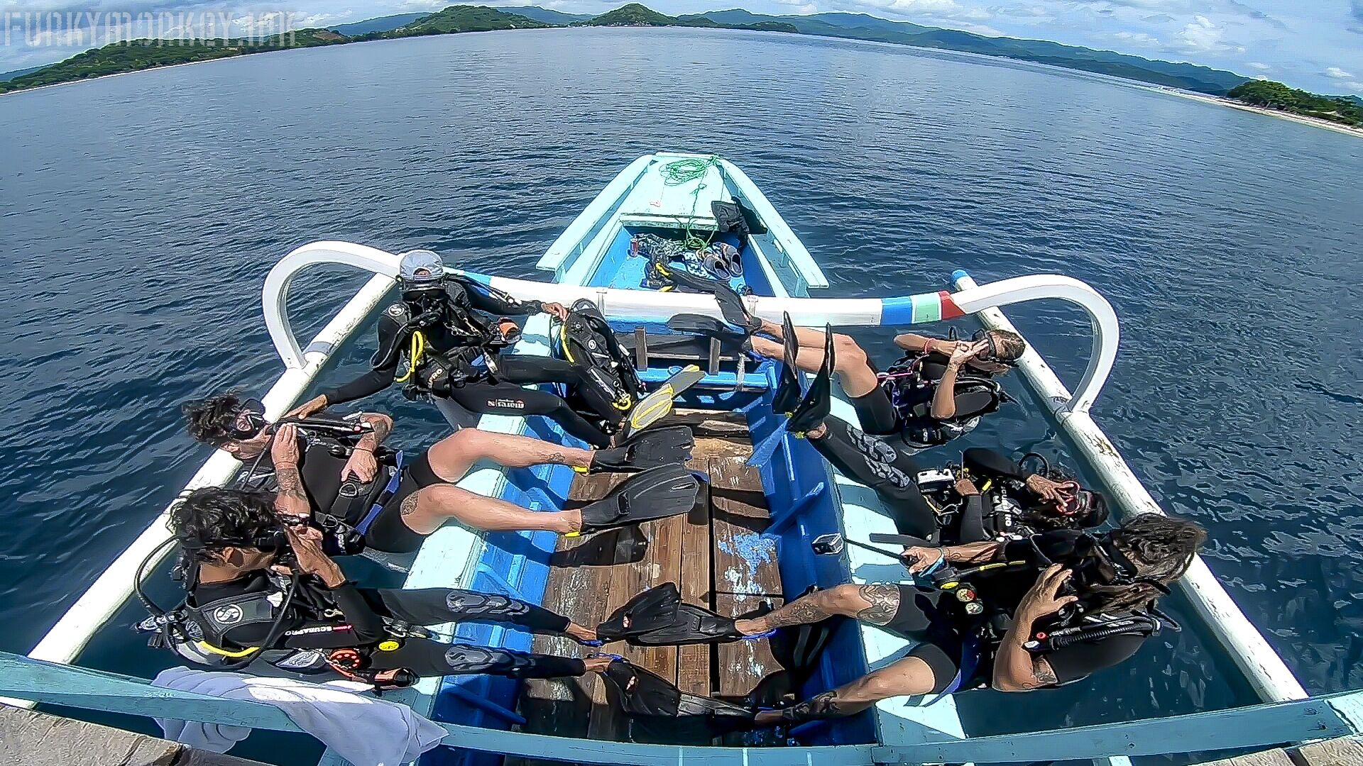Un bote con varios buceadores a bordo, equipados con equipo de buceo y cubierta de madera.