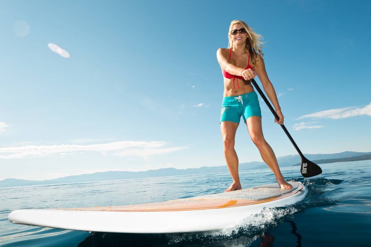 A person paddleboarding on a calm body of water with a clear sky and distant mountains in the background.