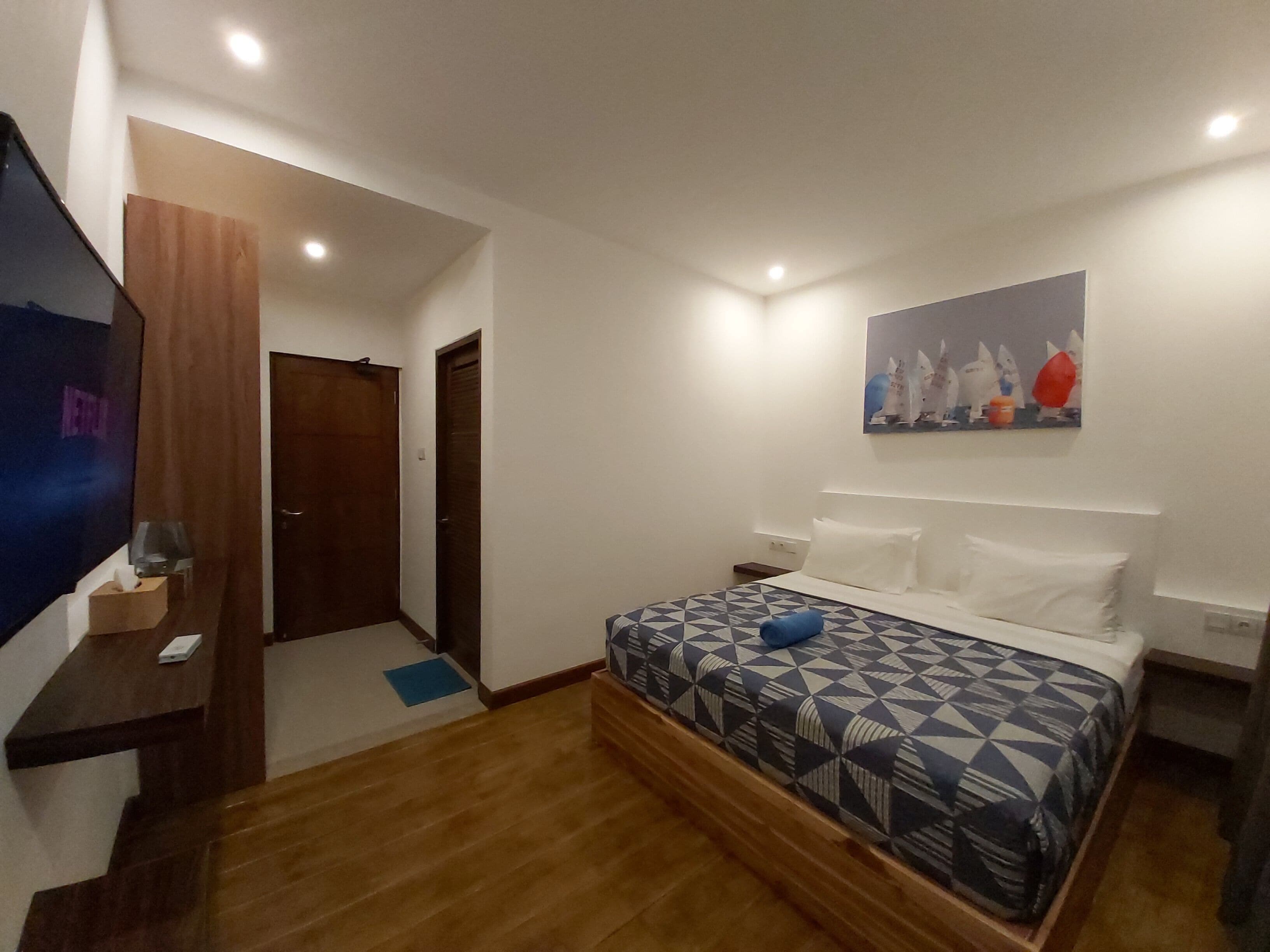 A bedroom with a bed, a TV, a painting, and a wooden floor.