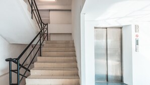 A staircase with beige tiles and black railings leading to an elevator with a metallic finish. - OYO Flagship 1170 The Habitat Karawaci (Curug)