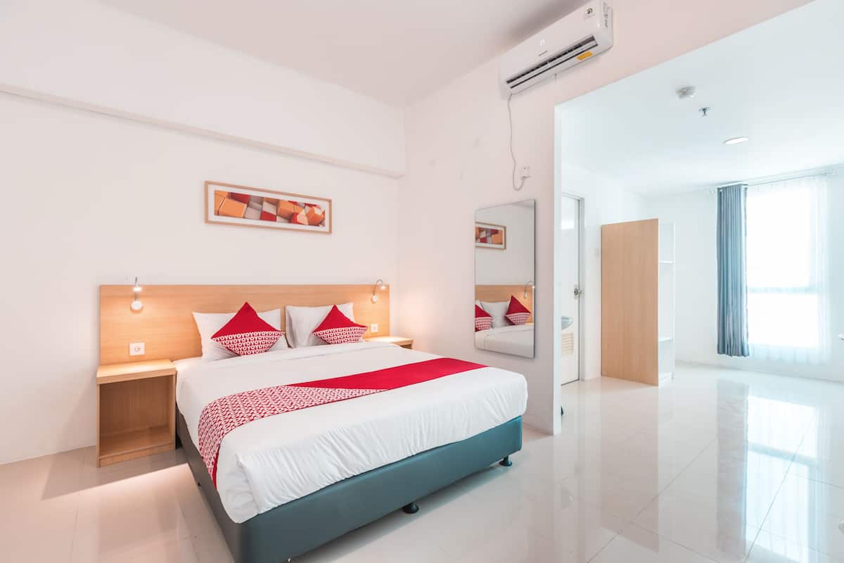 Ein modernes Hotelzimmer mit einem großen Bett, Nachttischen, einem Spiegel und einer Tür zu einem weiteren Raum.