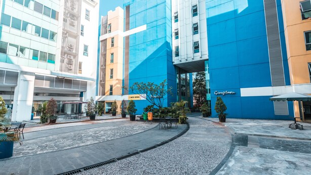 A modern building with a blue facade, a covered outdoor seating area, and a paved courtyard. - OYO Flagship 1170 The Habitat Karawaci (Curug)