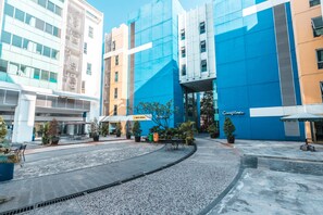 A modern building with a blue facade, a covered outdoor seating area, and a paved courtyard. - OYO Flagship 1170 The Habitat Karawaci (Curug)