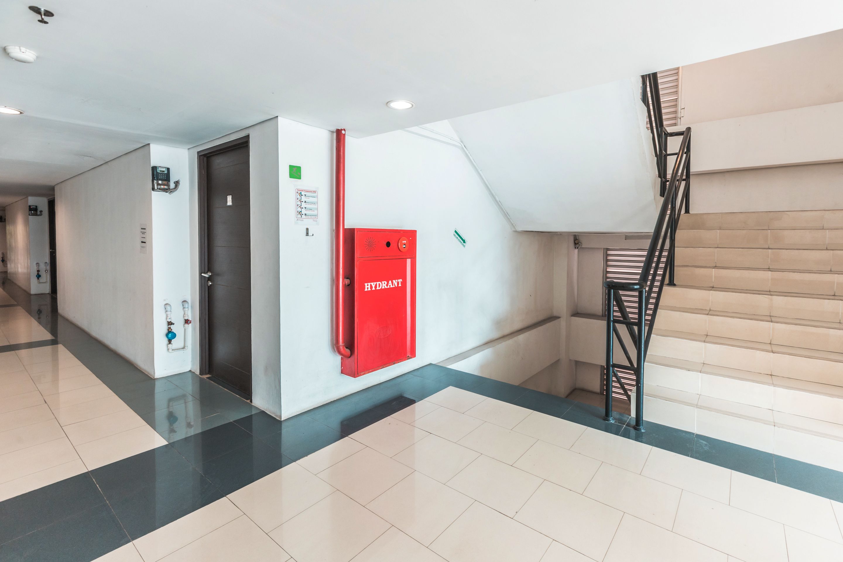Un couloir avec un potelet d’incendie rouge, une porte et un escalier.