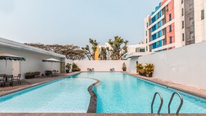 A swimming pool with a curved edge, surrounded by a white wall and a multi-story building with colorful facades. - OYO Flagship 1170 The Habitat Karawaci (Curug)
