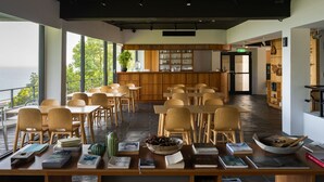 A spacious dining area with wooden tables and chairs, a central bar area with shelves of glassware, and large windows offering a view of the outdoors. - Day Spring (Nangan)