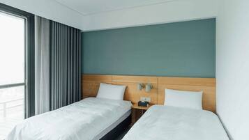 A hotel room with two single beds, a wooden headboard, a nightstand with a lamp, and a window with curtains.