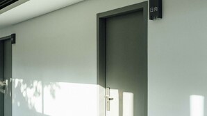 A modern hotel room with a minimalist design, featuring a large window and a door with a handle. - Day Spring (Nangan)