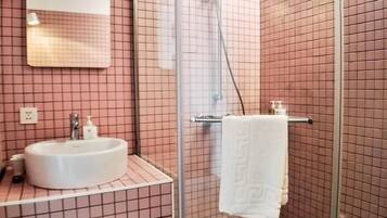 A bathroom with a glass-enclosed shower, a sink with a mirror above it, and pink-tiled walls.