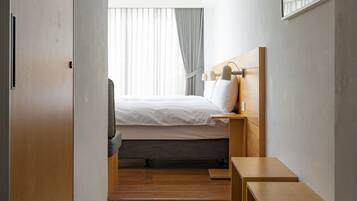 Ein modernes Hotelzimmer mit einem Bett, Nachttischen, einem Kleiderschrank und einem großen Fenster mit Vorhängen.