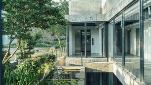 A modern building with a glass facade, a concrete structure, and a landscaped garden with trees and a water feature. - Day Spring (Nangan)