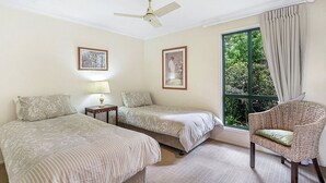 A room with two beds, a chair, a ceiling fan, and a window with curtains. - The Cottages (Tamborine Mountain)