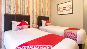 Habitación de hotel con dos camas, papel tapiz a rayas, un logotipo enmarcado en la pared y ropa de cama roja y blanca.