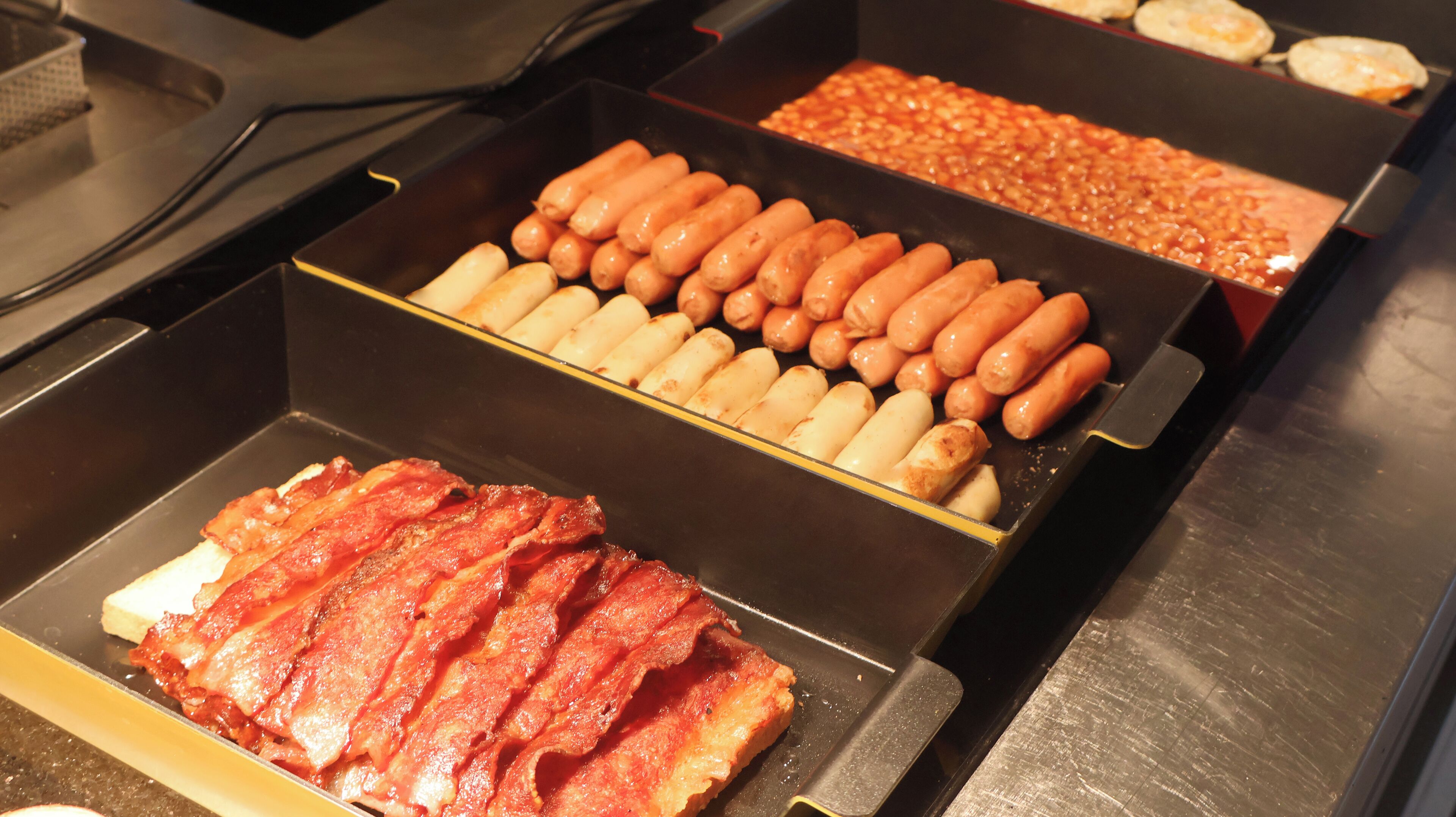 Un buffet proposant une variété de plats, notamment des saucisses, des haricots et du bacon.