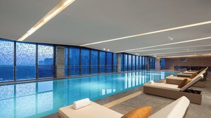 Una piscina interior moderna con sillones de descanso y vistas a la ciudad.