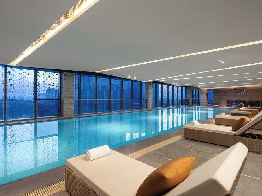 Une piscine intérieure moderne, dotée de chaises longues et offrant une vue sur la ville.