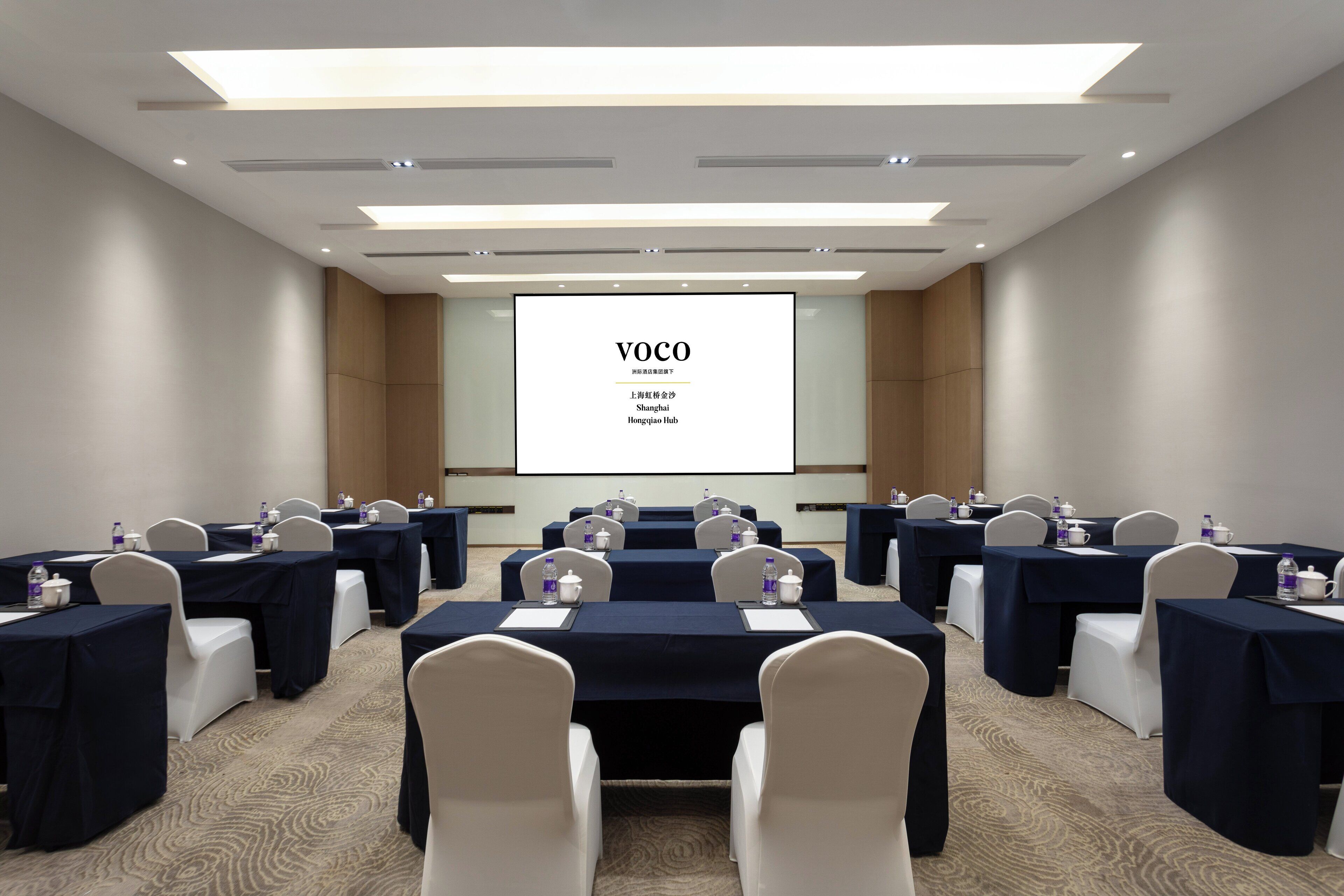 A conference room with tables and chairs, a projector screen displaying "VOCO", and a presentation screen.
