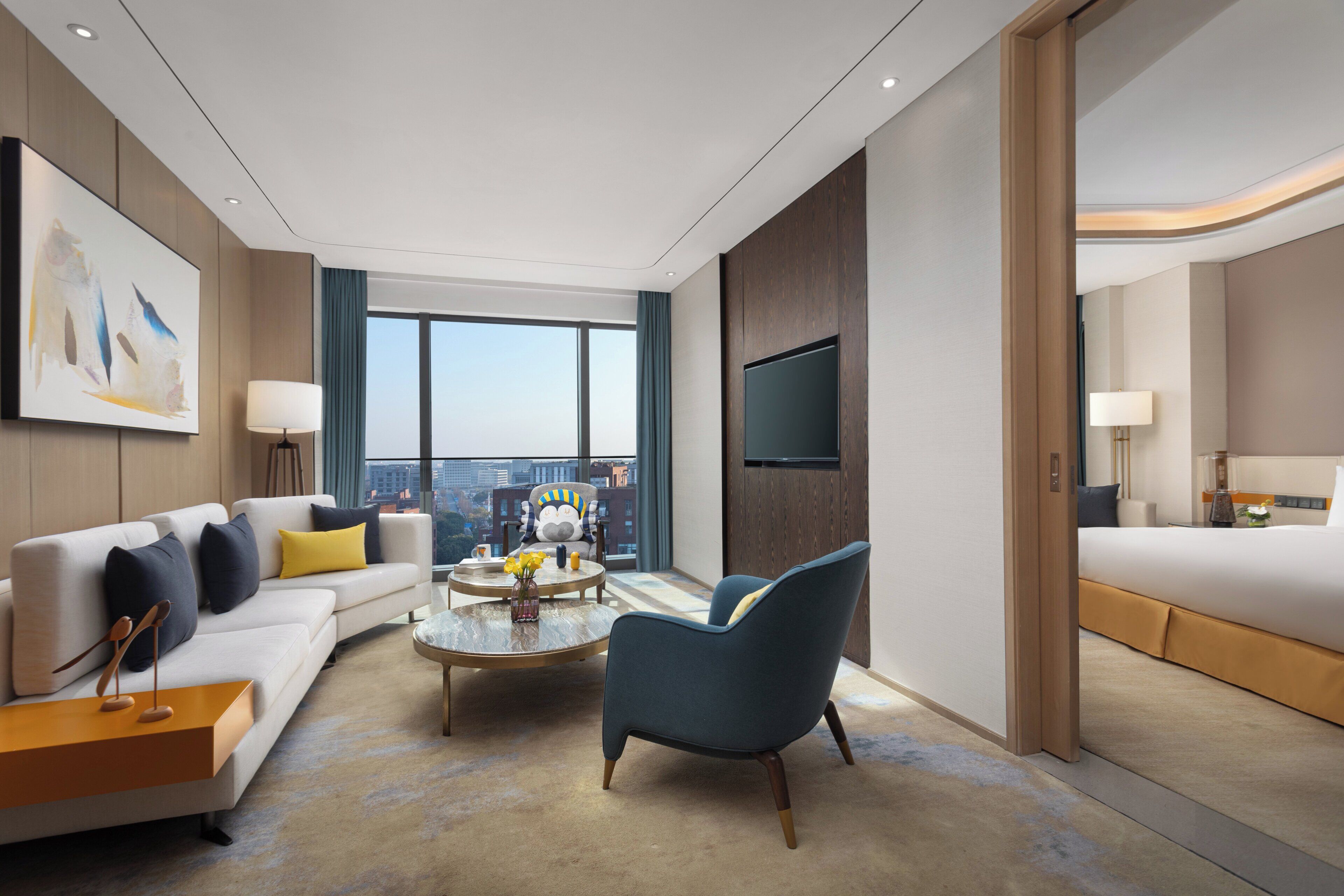 A modern hotel room with a sofa, armchair, coffee table, and a bed.
