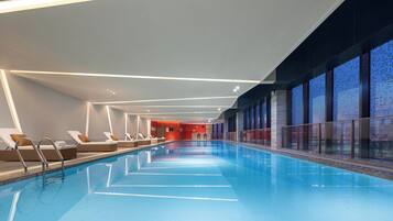 An indoor swimming pool with clear water, lounge chairs, and a modern architectural design.
