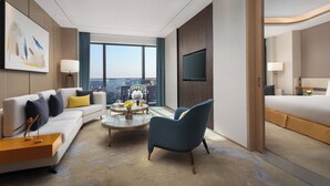 Una habitación de hotel moderna con sofá, sillón, mesita de centro y cama.