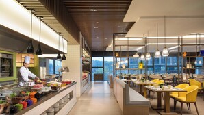 Un restaurante moderno con un chef preparando comida, una zona de buffet y sillas amarillas.