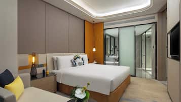 Ein modernes Hotelzimmer mit einem großen Bett, einer Couch, einem Nachttisch, einer Lampe und einer Vase mit Blumen.