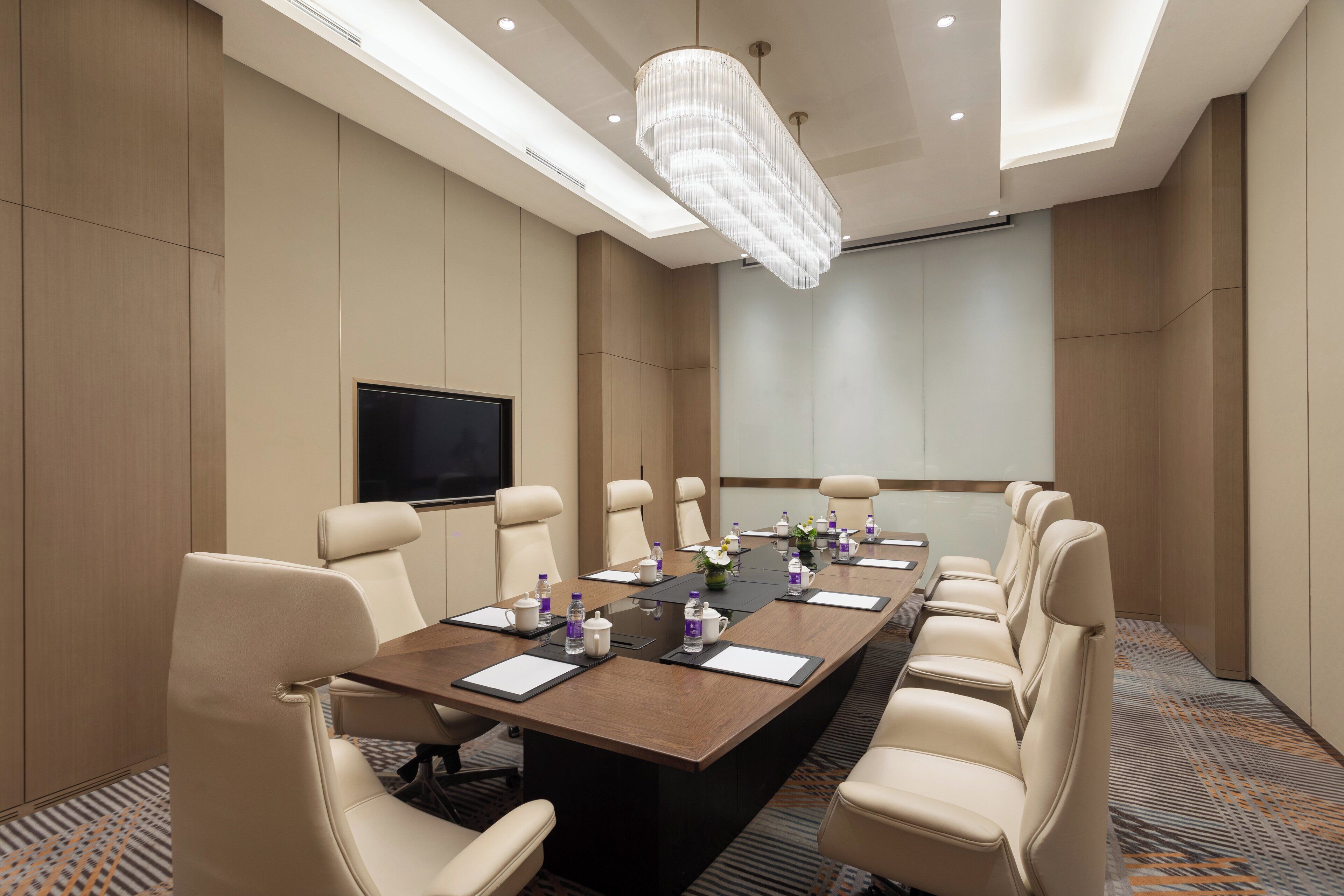 A conference room with a long table, multiple chairs, a flat-screen TV, and a chandelier.