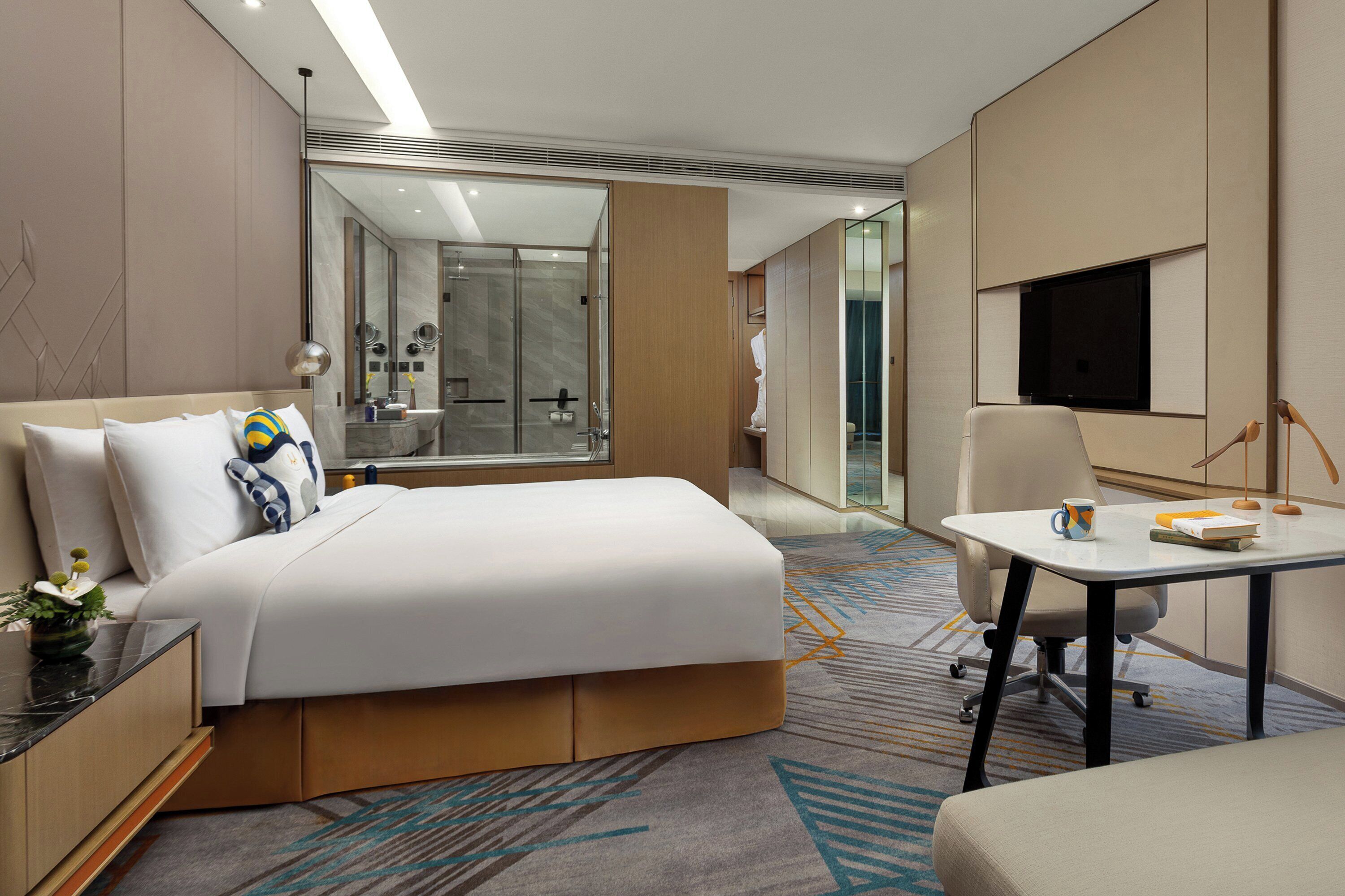 Een moderne hotelkamer met een groot bed, een bureau met stoel, een televisie, en een badkamer zichtbaar door een geopende deur.