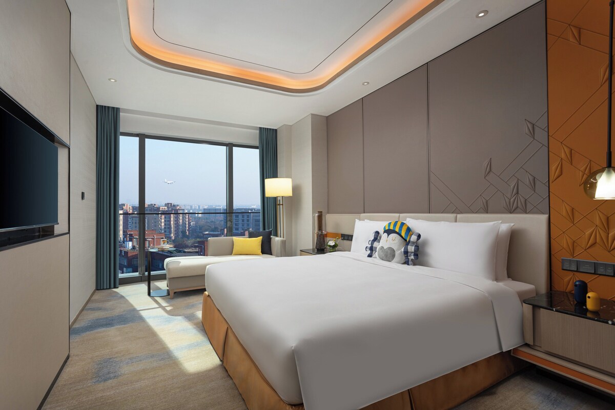 Habitación de hotel moderna con una cama grande, televisor de pantalla plana, sofá y vista a la ciudad.