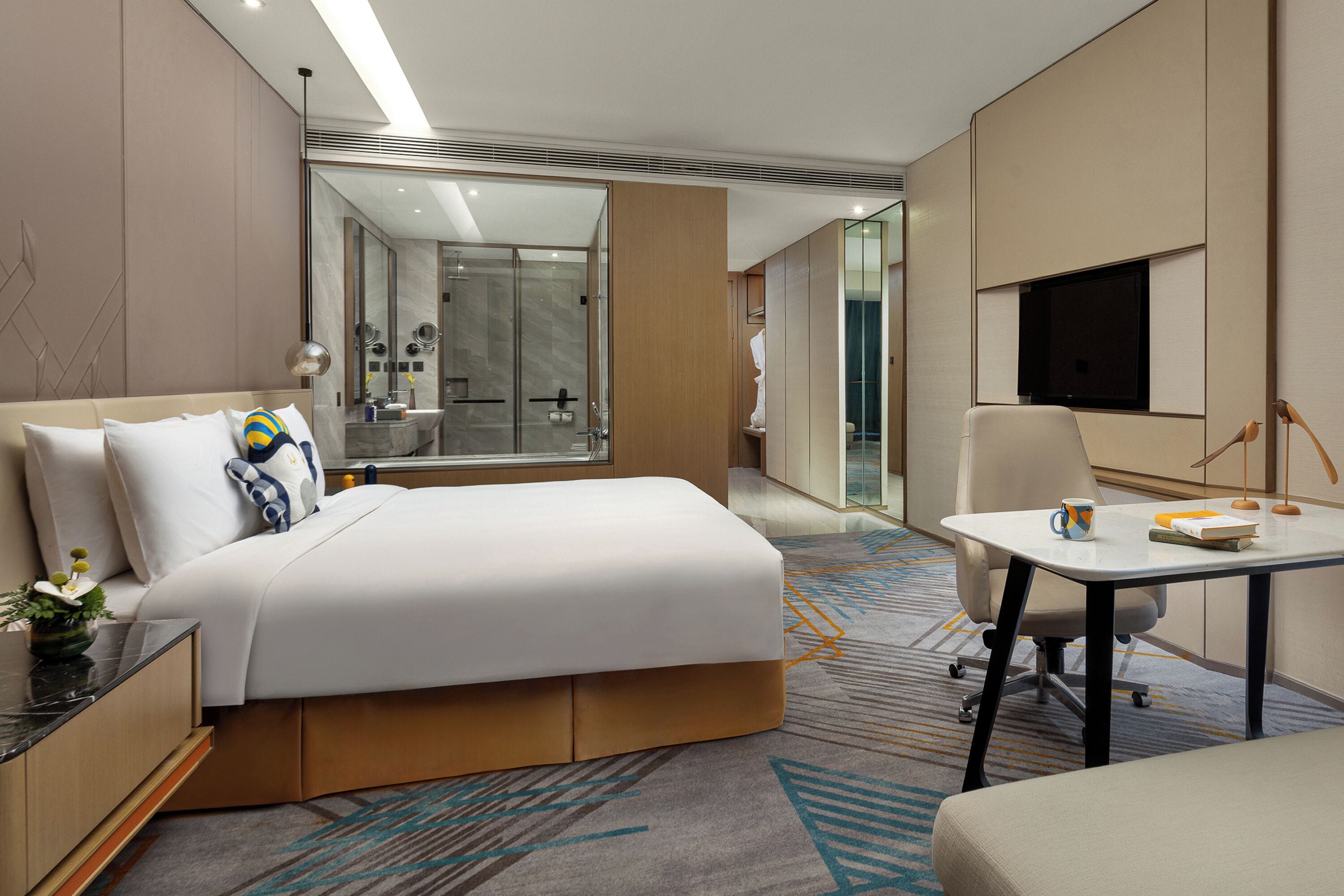 A modern hotel room with a large bed, a desk, a chair, and a TV.
